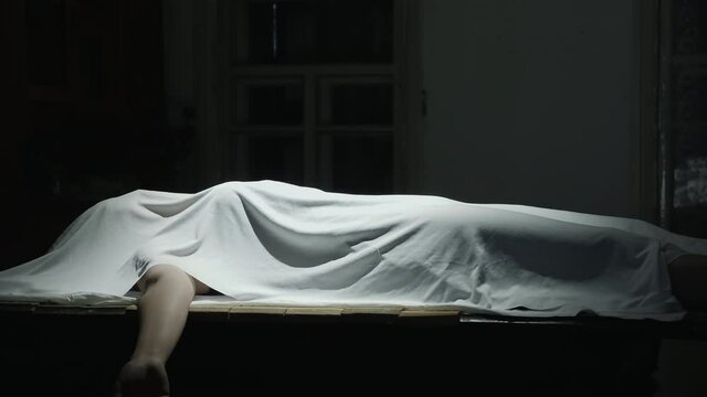 Dead body covered with a white cloth in the darkroom with swinging a light