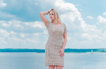 Nice blonde romantic plus size woman in knitted fashionable golden dress at seafront, fashion concept, fancy clothes 