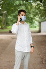 A young man in a mask talking on the phone outdoors