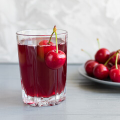 Cherry juice in a glass cup with cherry berries on a plate on a gray table. Selective focus.