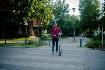 Young modern man using and driving electric scooter on city street. Modern and ecological...