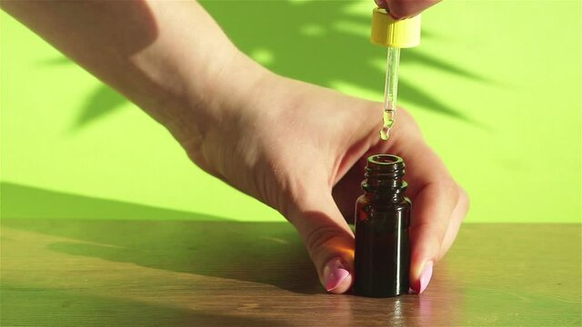 woman hand using dropper with natural  cbd hemp oil dripping in to glass bottle close up on green background