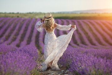 pretty blonde woman running away in lavender field. woman in long dress and straw hat having fun in flowers of lavender - 365429645