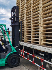 Worker driving forklift to loading and unloading wooden pallets from truck to warehouse cargo storage, shipment in logistics and transportation industrial, wood pallets stack
