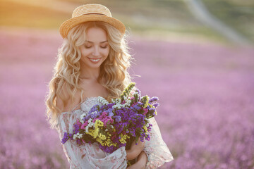 pretty blonde woman running away in lavender field. woman in long dress and straw hat having fun in flowers of lavender