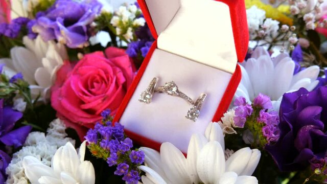 Top view of gift present red box with a set of engagement ring and earrings on the background of a multi-colored beautiful bouquet of flowers. Marriage proposal, a new happy life