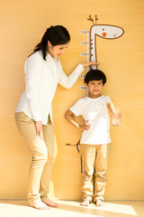 Young mother measuring height for son at home