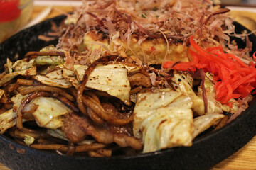 Close-up of the Okonomiyaki, Japanese Pizza topped with bonito flakes and sliced-pickled ginger in a hot iron frying pan in Kyoto, Japan