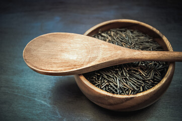 Wooden bowl with black rice and spoon  at wooden background. Raw vegan organic grain food.