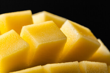 Macro shot of the fresh mango tropical fruit cut in cubes on the dark background