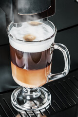 glass cup with hot cappuccino with foam prepared in the coffee machine
