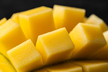 Macro shot of the fresh mango tropical fruit cut in cubes on the dark background