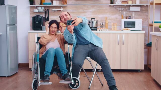 Boyfriend taking selfie with happy and disabled wife in wheelchair. Hopeful husband with handicapped disabled disability invalid paralysis handicap person next to him, helping her to reintegrate
