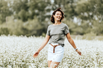 Portrait of a beautiful young woman  runs across the field with white flowers, enjoying the day, on a sunny summer day. 