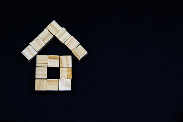 Obraz na płótnie Canvas A house of wooden blocks on a dark background. The the concept of real estate, house building, insurance, housing, family. The roof and walls from cubes