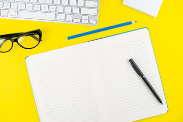 Fototapeta na wymiar Keyboard, pen, black eye glasses, pencil, notepad planner on yellow background. Flat lay. Copy space. Workplace in the office.