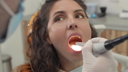 Back view of male dentist wearing medical mask and gloves checking teeth health of young woman lying on dental chair using special tool