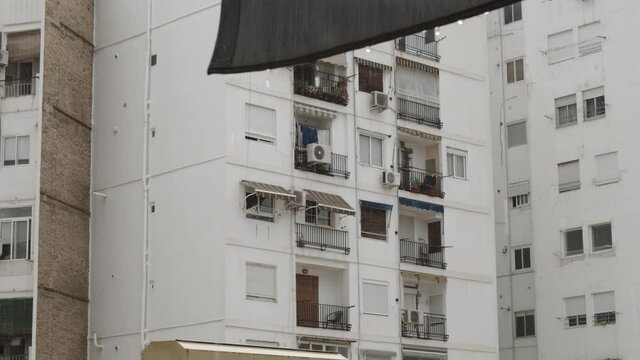Looking at neighboring white facade apartment house with empty balconies in the rain. Raindrops falling from sunshade