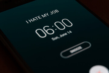 On a black smartphone, an alarm clock rings for 6 am with the inscription I hate my job close-up, background