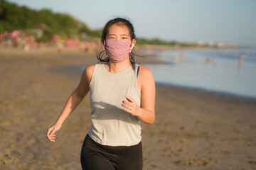 new normal running workout of Asian girl in face mask - young happy and beautiful Japanese woman jogging on the beach in post quarantine outdoors exercise