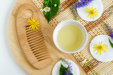 Small white bowl with cosmetic (massage, cleansing) aroma oil, wooden hair brush, cotton pads and wild flowers. Natural skin care, homemade spa and beauty treatment recipe. Top view, copy space.