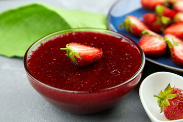 Strawberry confiture in glass bowl with fresh ripe strawberries on grey concrete table background.