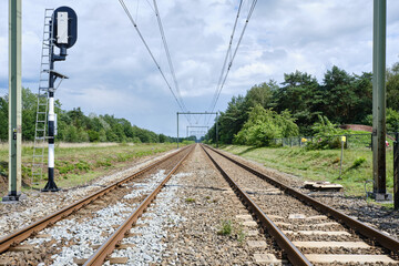 Two railway tracks with electric power cables and on the left side a train signal pole into the...
