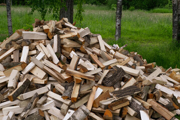 A large pile of firewood on the meadow. Trees/timber has been cut and split into firewood to be used as fuel for heating in fireplaces and furnaces in the.