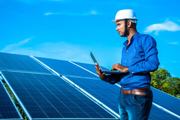 Young male engineer with laptop in hand standing near solar panels, agriculture farm land with...