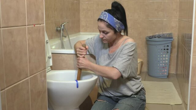 Woman using plunger to unclog a toilet bowl