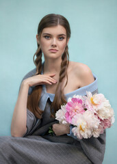 Art photo of a rustic tender girl with a bouquet of peonies on a blue background