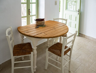 A simple white kitchen table with wooden surface and white chairs in a country house with door and...