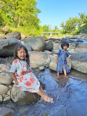 Asian kid girls are standing and playing on the river and rocks in the beautiful village