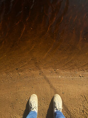Sneakers on the border of land and water. Shoes top view near the water.