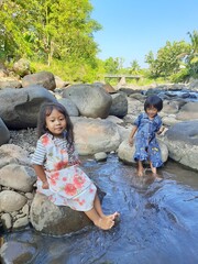 Asian kid girls are sitting and playing on the river and rocks in the beautiful village,they are on vocation