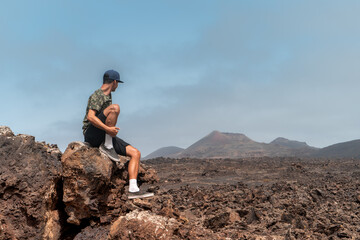 Hombre joven se sienta sobre una roca de lava a contemplar el Parque Nacional de Timanfaya. Lanzarote. Islas Canarias