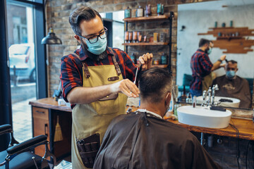 Hair cutting during pandemic. Young man have hair cutting at barber shop during pandemic isolation, they both wear protective equipment.