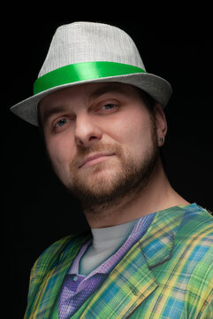 handsome bearded confident man in grey stylish hat with green ribbon looking at camera on black 