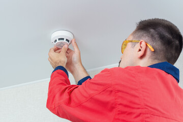 Worker mounting fire alarm or smoke detector on the ceiling