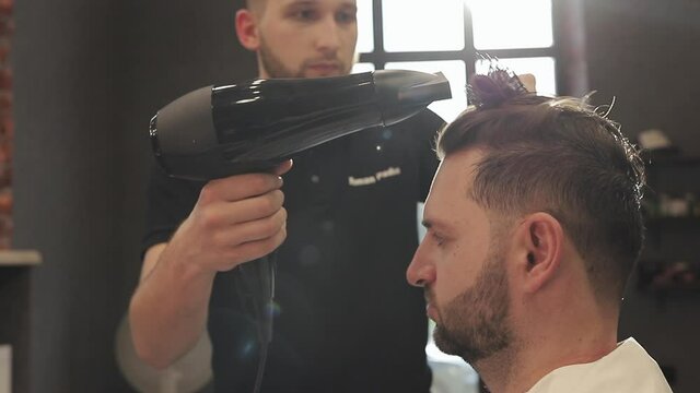 Professional and proper hair care. Cutting hair and beard. Hairdresser making hairstyle in male salon. Barber with dark hair wearing black gloves doing a haircut for client at barber shop