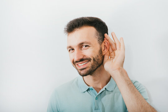 Check your hearing. Positive man holds his hand near his ear, on a gray background. Ear health, treatment and diagnosis of hearing
