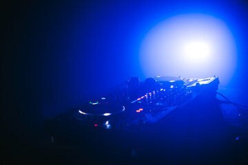 Headphones on DJ mixer console board panel in night club with blue light and smoke.