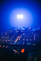 Close up of Headphones on Disc jockey mixing board in night club with blue light and smoke.