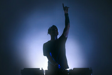Black silhouette of a Male Disc jockey playing music raising an arm up.