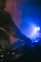 Arms of a Disc jockey playing the mixer with a blue smoke lighting.