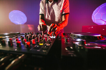 Close up of hands of a male DJ playing the mixer table for techno music in a dark colorful...