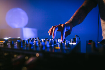 One hand of a male Caucasian DJ playing music on a mixer board in a blue atmosphere. Close up shot.