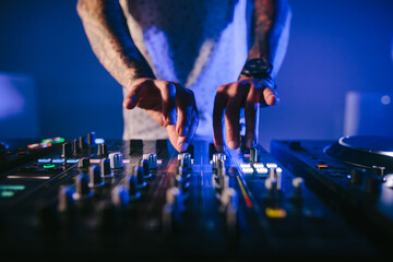 Hands of a male DJ playing music in a blue background.