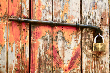 Old rusty padlock on wooden door. Shabby barn gate with a lock and piece of rusty metal. Material: wood with pale orange paint