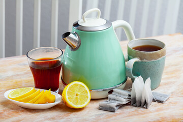 New teapot on table with cup of black tea and sliced lemon in home interior, nobody..